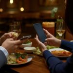 Due persone cenano al ristorante con lo smartphone in mano